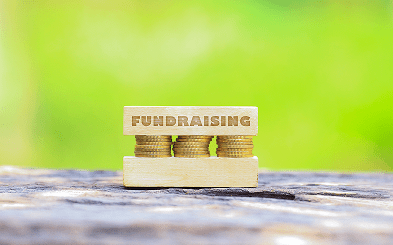 Stacked coins with a wooden block labeled 'FUNDRAISING' symbolizing financial support.